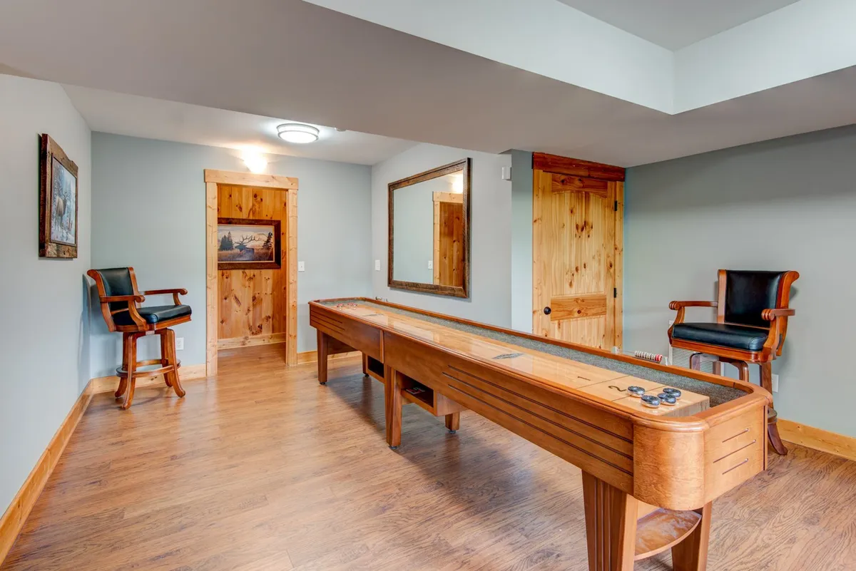 This image showcases a game room featuring a shuffleboard table, wooden chairs, and framed artwork on the walls. The space feels relaxed and inviting, ideal for friendly competition and group entertainment.