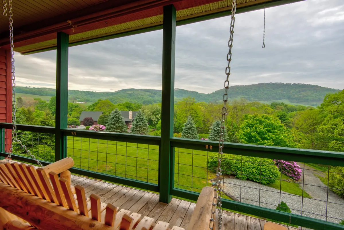 A cozy swing bench sits amidst lush greenery, with distant hills and the house visible in the background. The scene evokes tranquility and encourages outdoor relaxation, with the bench serving as a spot for peaceful moments or enjoying the views with a pet.