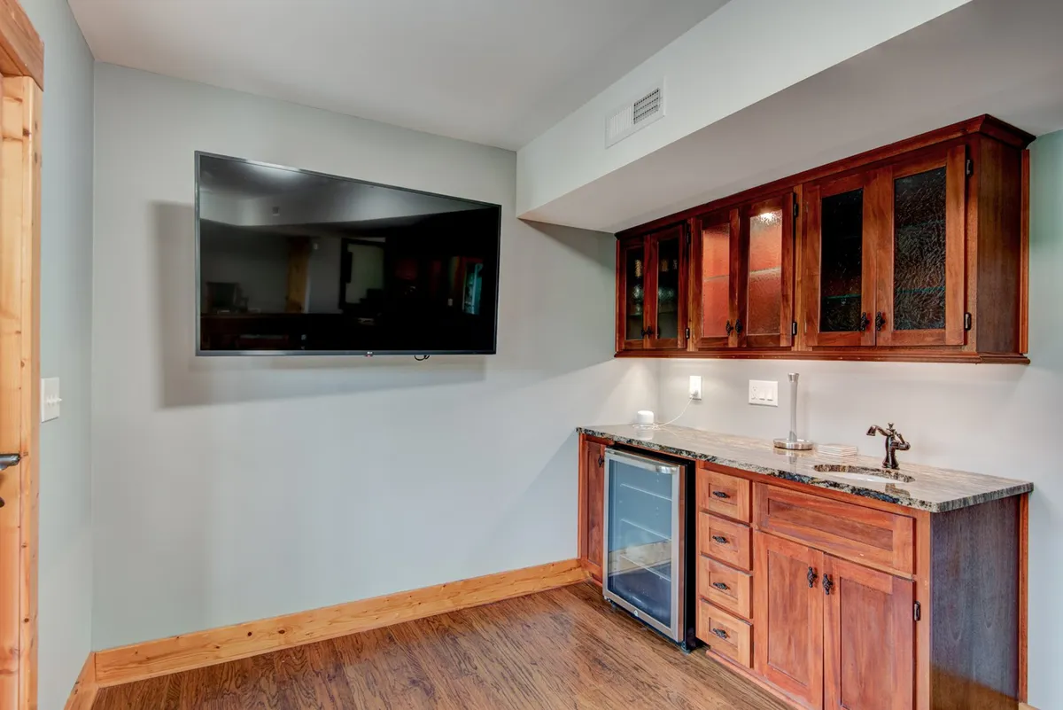 A cozy interior featuring a television, a bar area, and wooden cabinetry. The setup suggests a space perfect for watching sports or movies, pouring a glass from the wet bar, and socializing with guests.