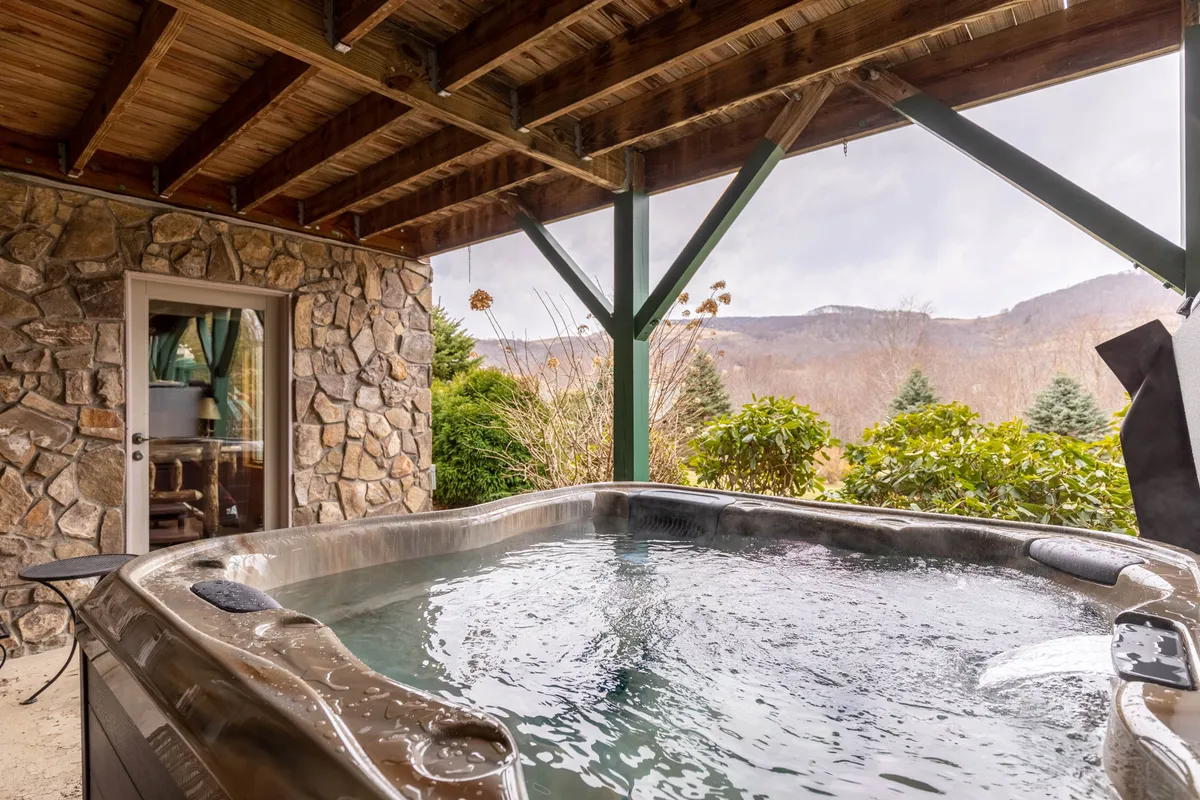 An outdoor hot tub set against a stone wall with views of lush greenery and distant mountains. The scene evokes relaxation, with the promise of soaking under the stars or unwinding in nature.
