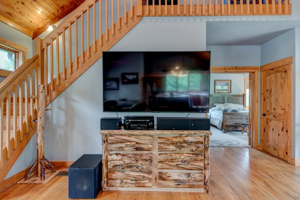 A cozy living area anchored by a large smart TV and wooden media console, with an inviting seating arrangement and a staircase in the background. The space is ideal for movie marathons, game nights, and family time.
